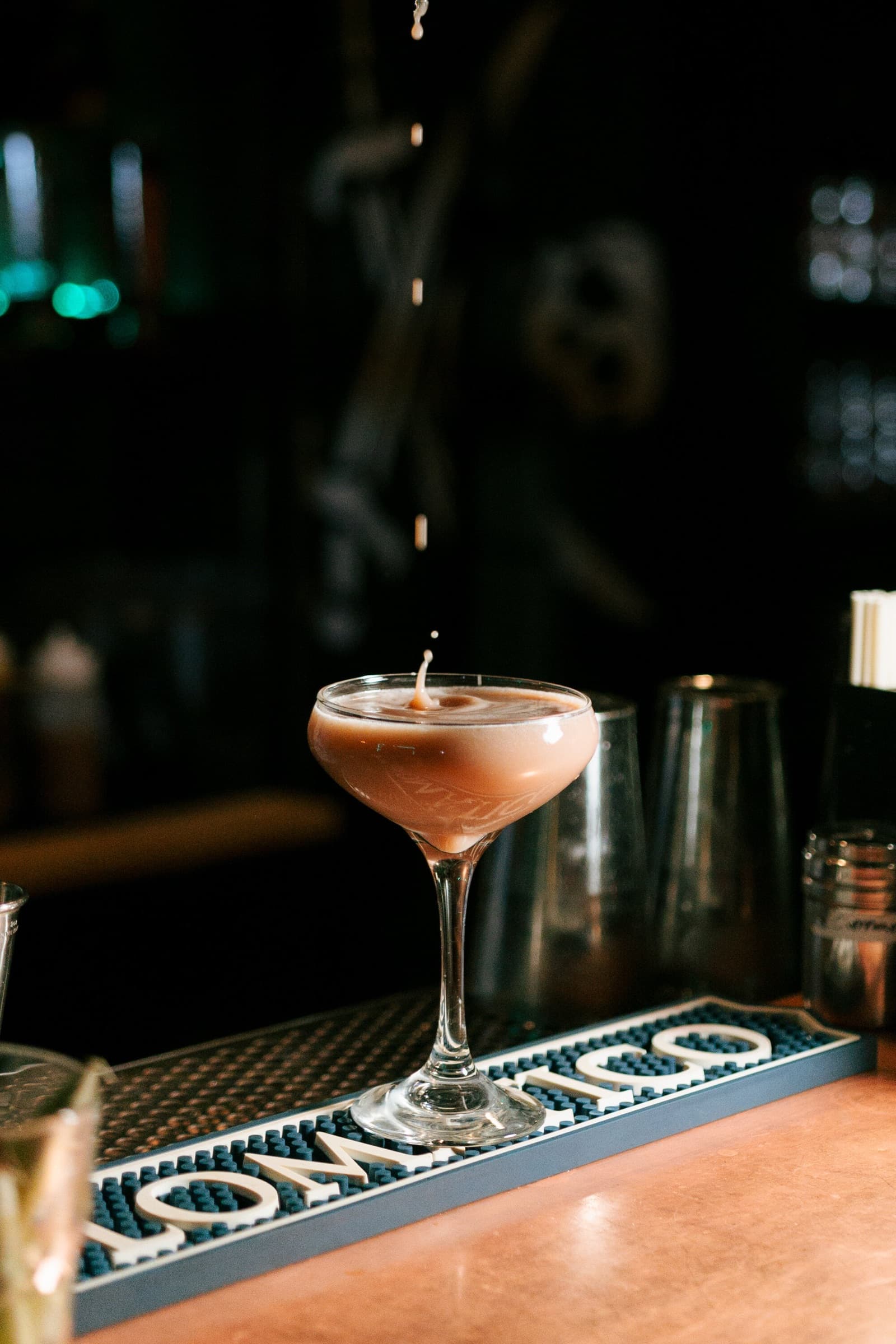 A coupe glass with a drop falling into the drink, on a Momoku bar mat